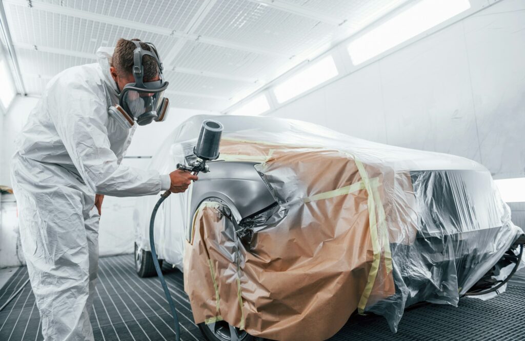 Painting job in progress. Caucasian automobile repairman in uniform works in garage